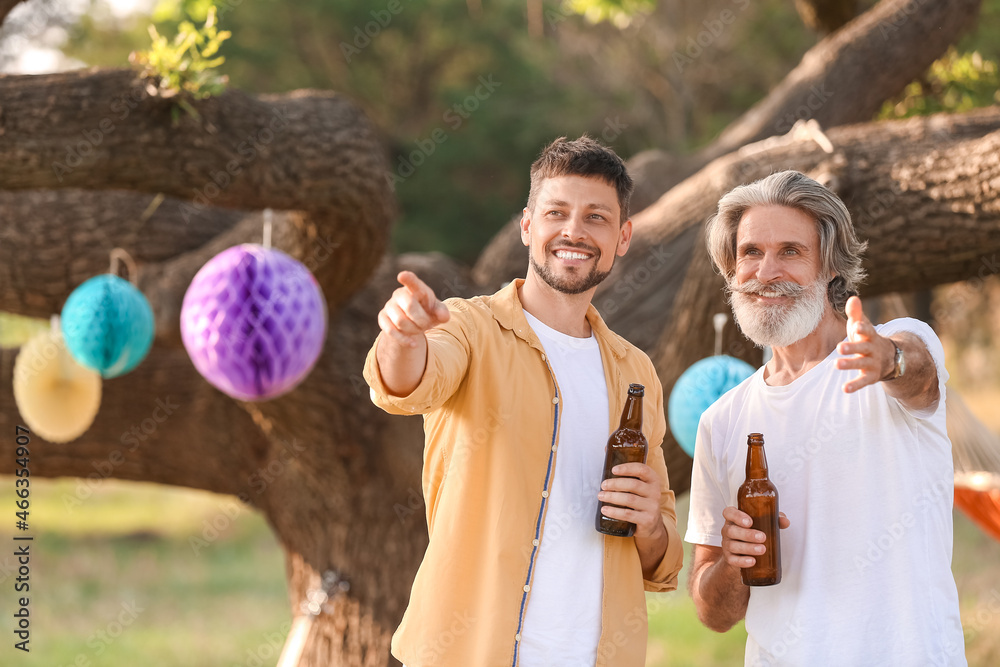 快乐的男人和他的父亲在夏天的烧烤派对上喝啤酒