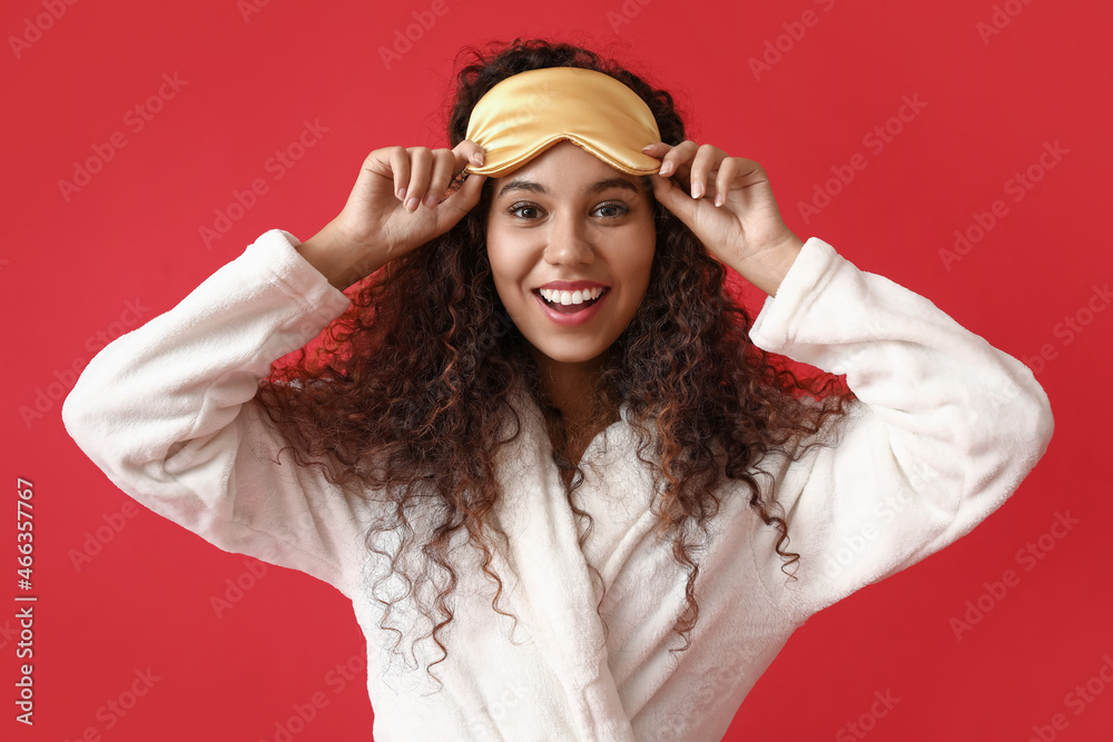 Young African-American woman with yellow sleeping mask on red background