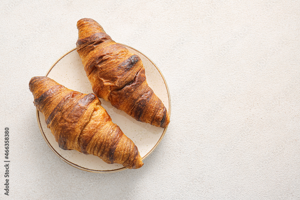 Plate with tasty homemade croissants on light background