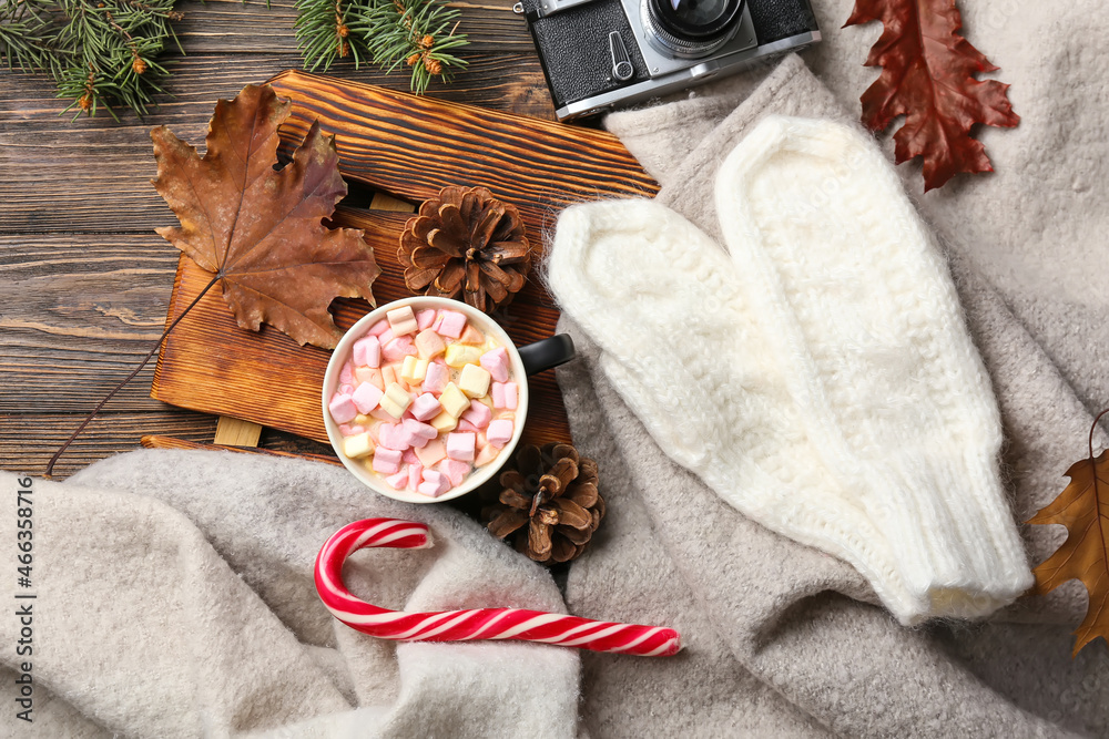 Cup of cocoa with marshmallows, candy cane and mittens on dark wooden background