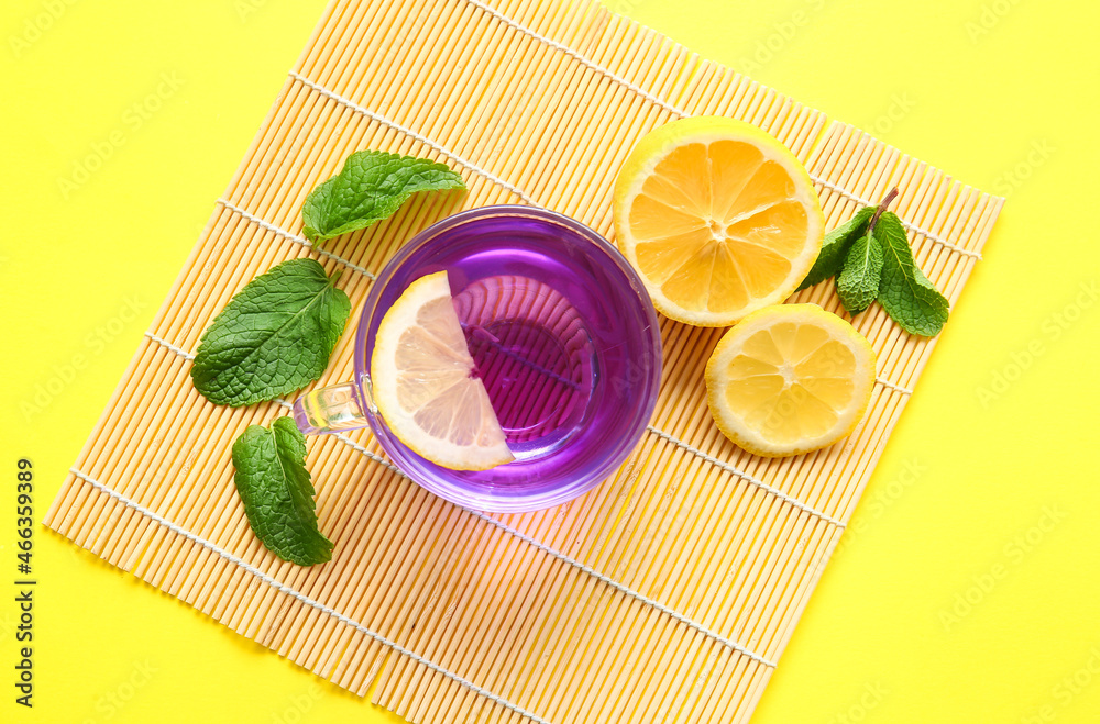 Mat with glass cup of organic butterfly tea and lemon on color background