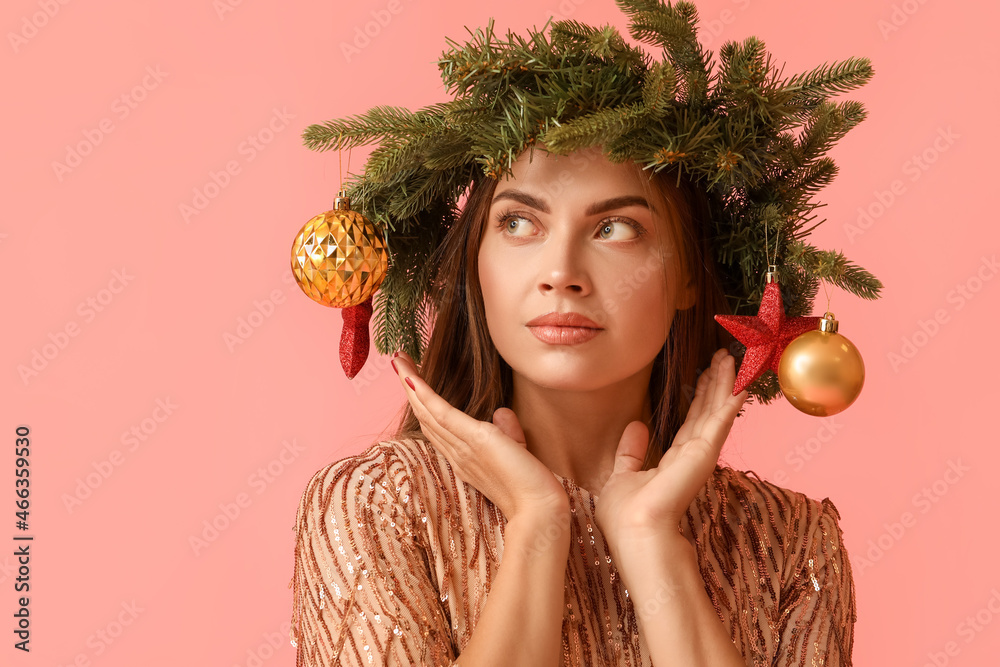 Beautiful young woman in wreath with Christmas decor on pink background