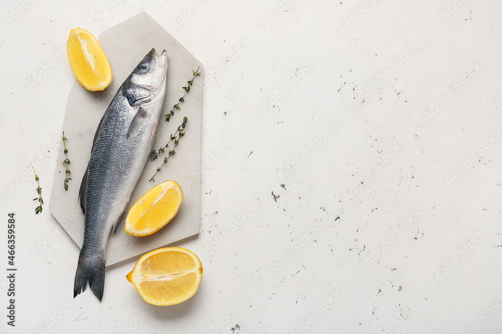 Board with fresh uncooked sea bass fish and lemon on white background