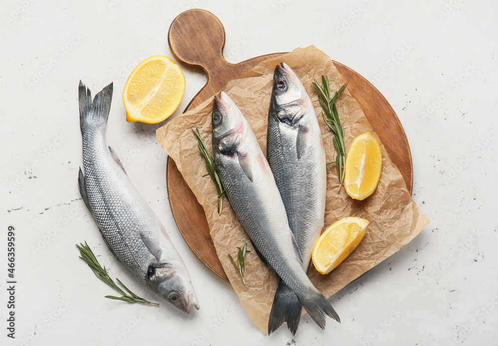 Wooden board with fresh uncooked sea bass fish on white background