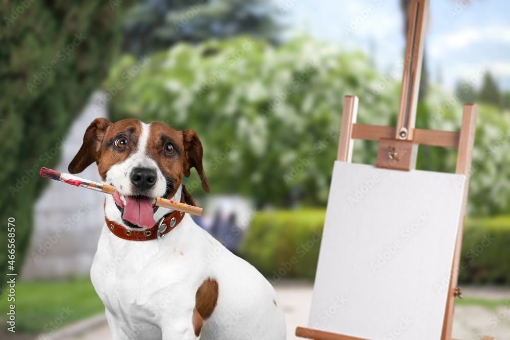 Dog artist. A pet sits near an easel with a white blank paper and holds a brush in its teeth.