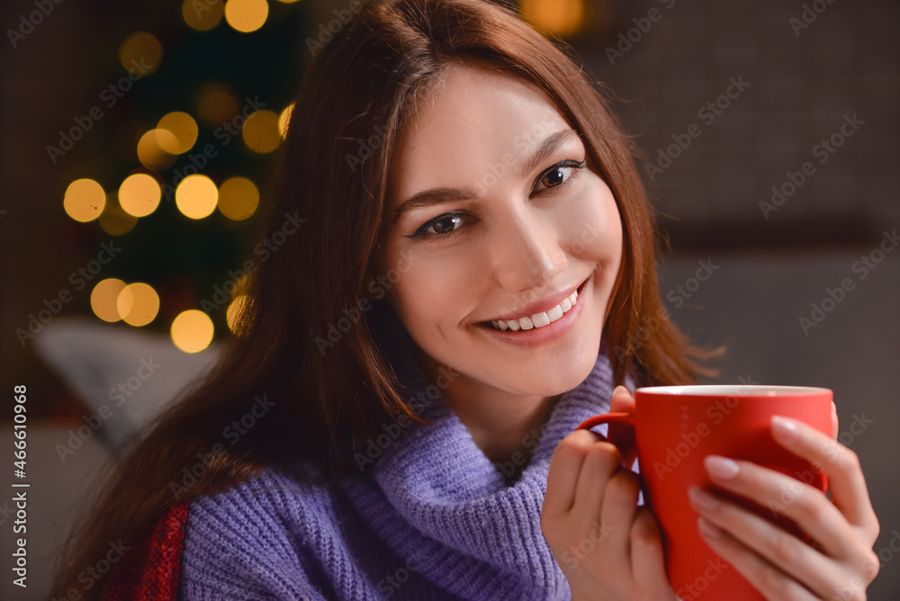 Beautiful young woman with cup of hot cacao drink at home on Christmas eve