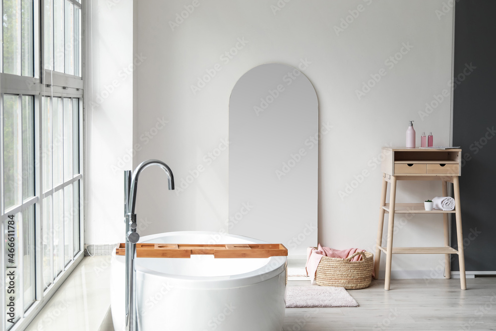 Modern bathtub and big mirror in white room