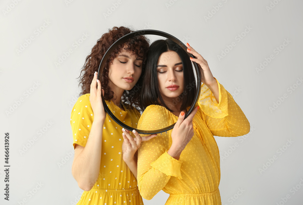 Young sisters with closed eyes holding round frame on grey background