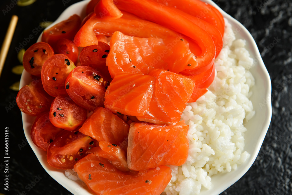 Tasty poke bowl with salmon and vegetables on dark background, closeup