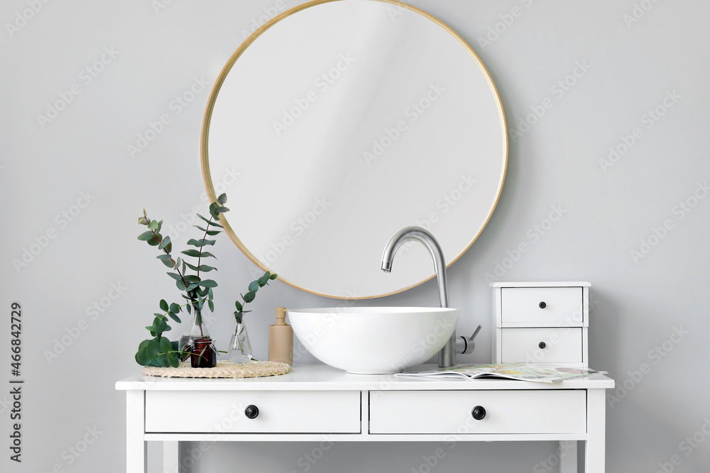 Vases with green eucalyptus branches and sink on table in bathroom