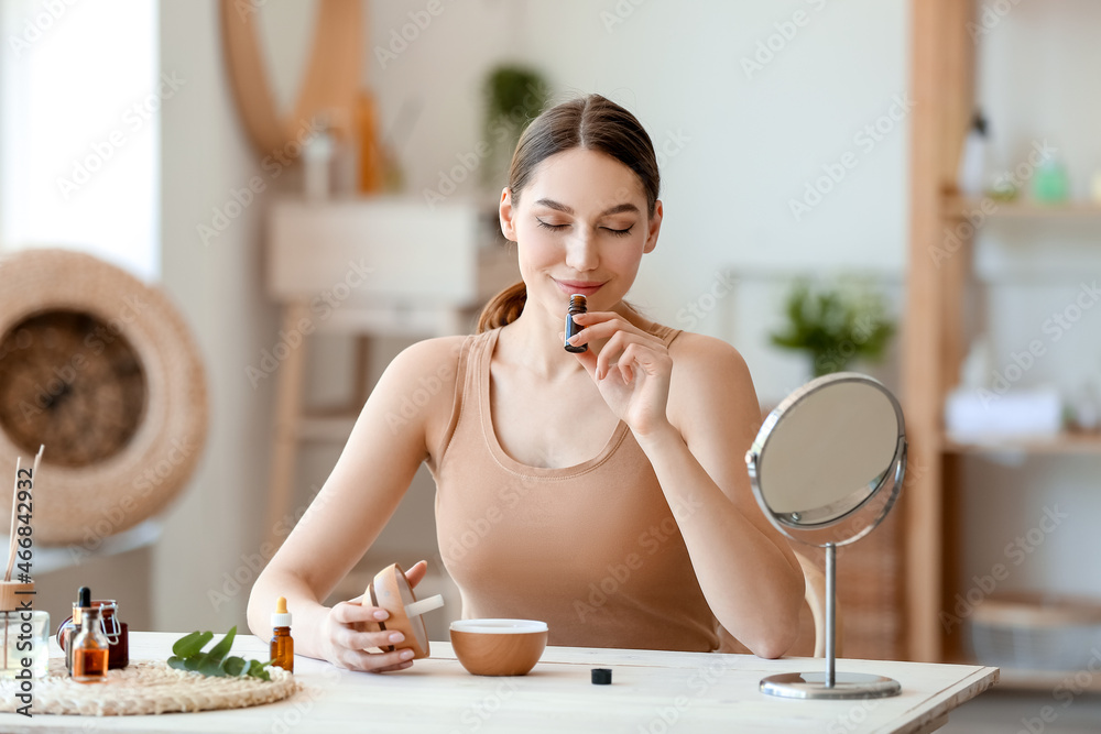 年轻女子坐在桌子旁，闻着瓶子里的天然精油