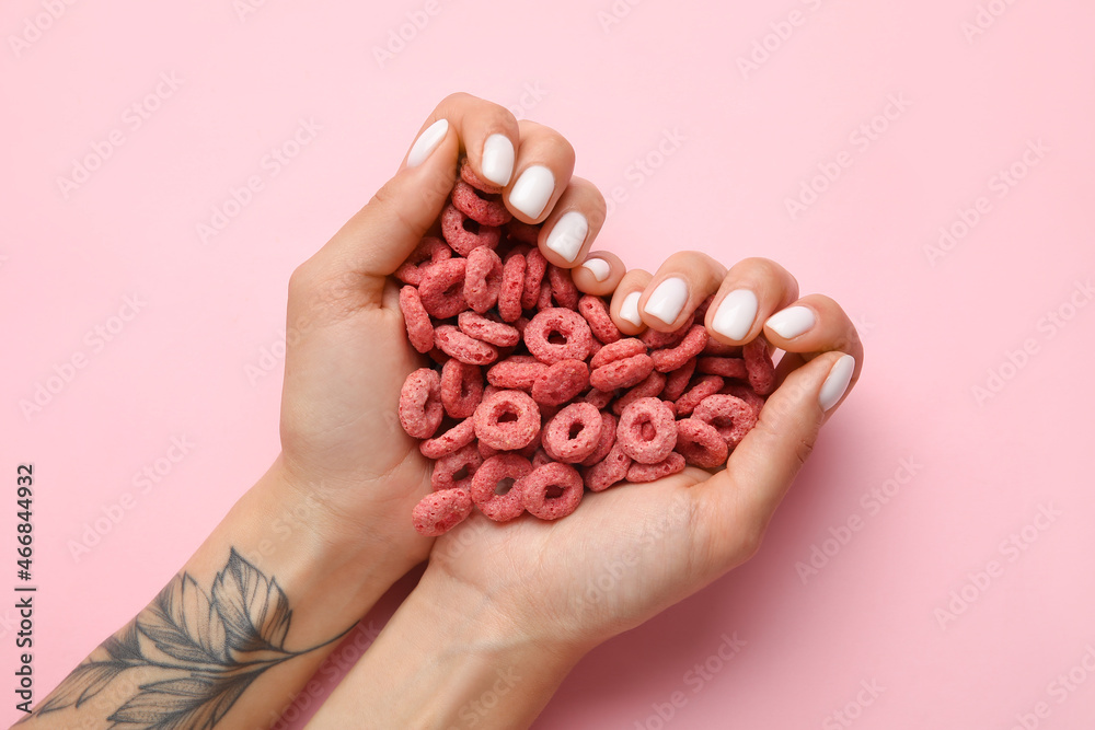 Woman with beautiful manicure holding cereal rings on pink background