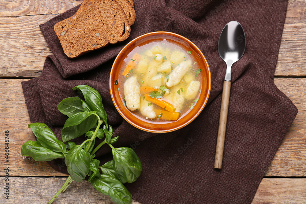 Bowl of tasty dumpling soup, bread and basil on wooden background