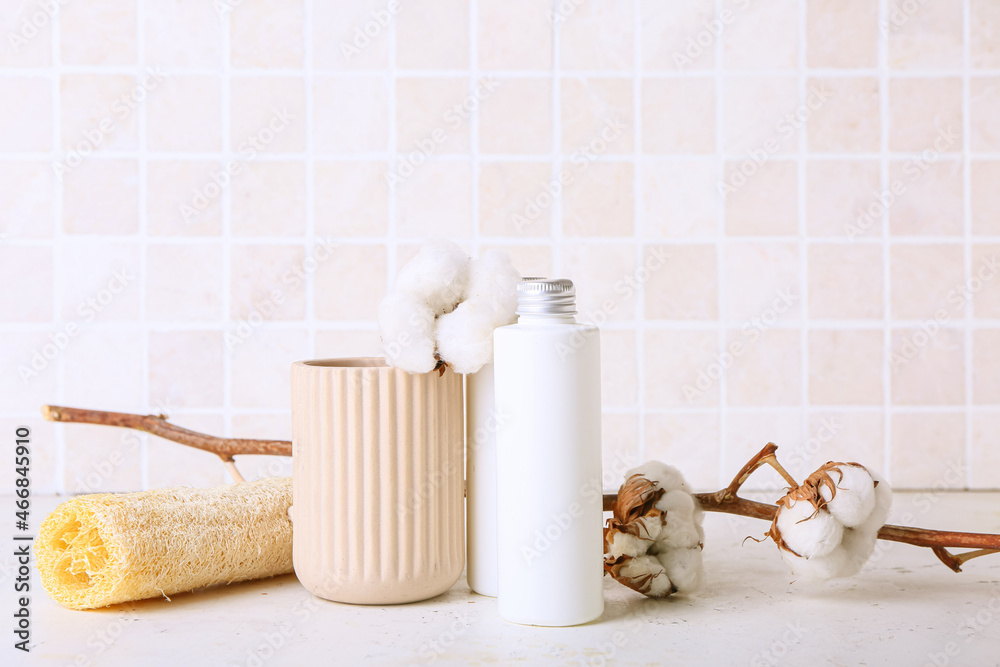 Bottle of cosmetic product, sponge and cotton branch on table against tile wall