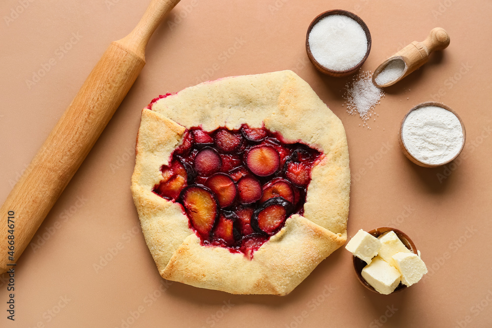 Tasty plum galette, butter, sugar and flour on color background