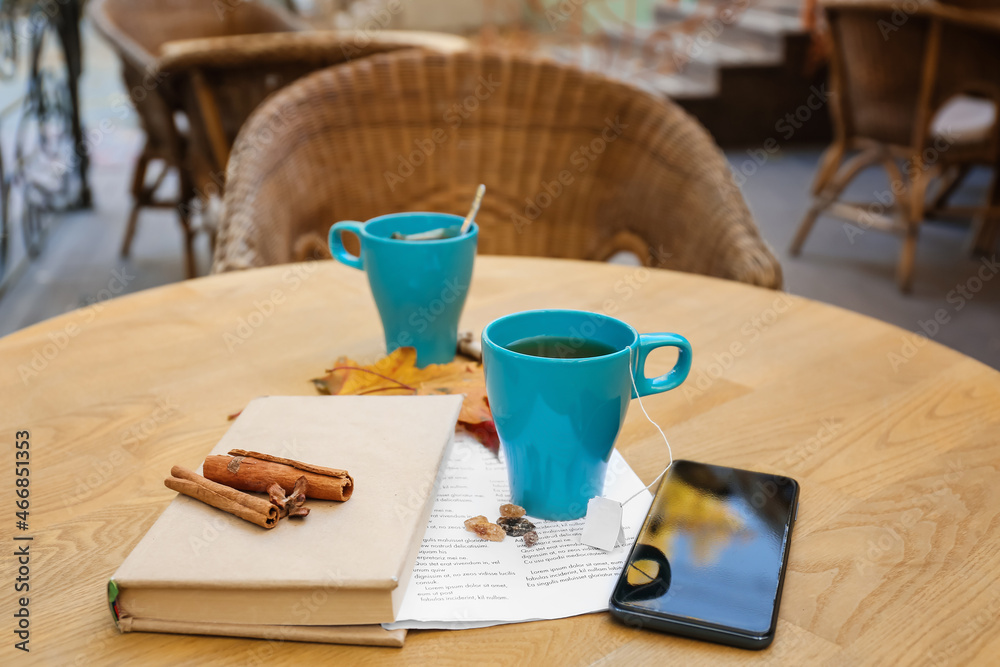 Blue cup of hot tea with book and mobile phone on table in cafe