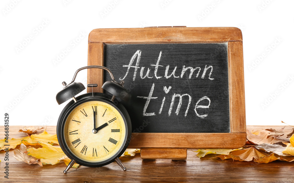 Alarm clock, chalkboard and autumn leaves on table against white background. Daylight saving time en