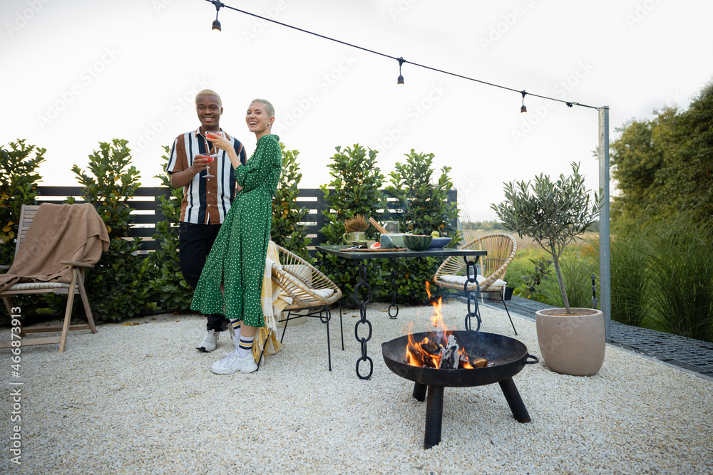 Multiracial couple hanging out together during a dinner at their backyard in the evening. Standing w