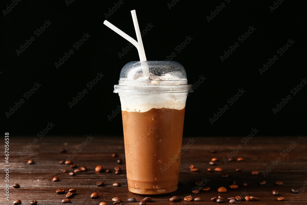 Plastic cup of tasty iced coffee with cream and beans on table