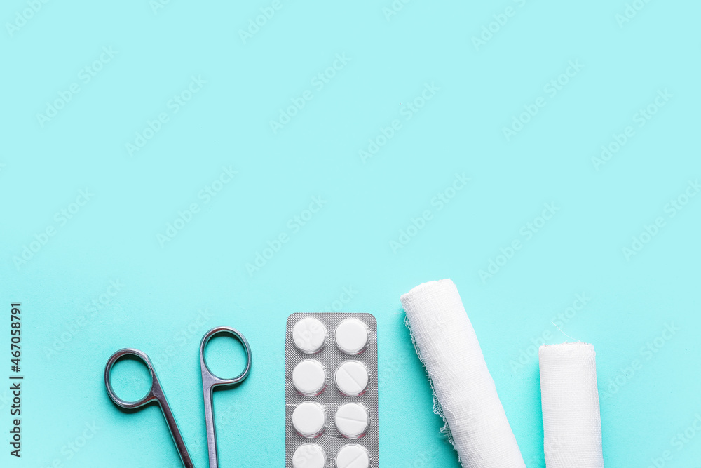 Surgical scissors, pills and medical bandage rolls on color background, closeup