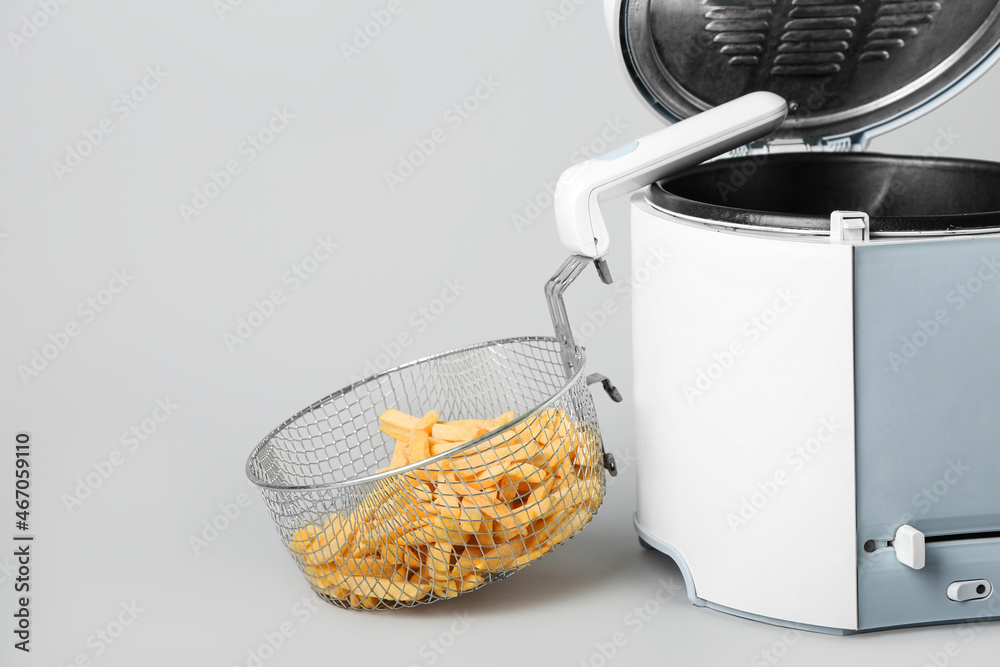 Modern deep fryer with french fries on light background