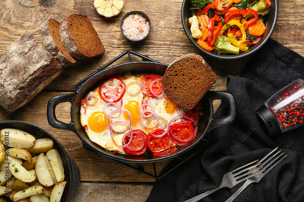 Baking dish with tasty Shakshouka, vegetables and fried potatoes on wooden background