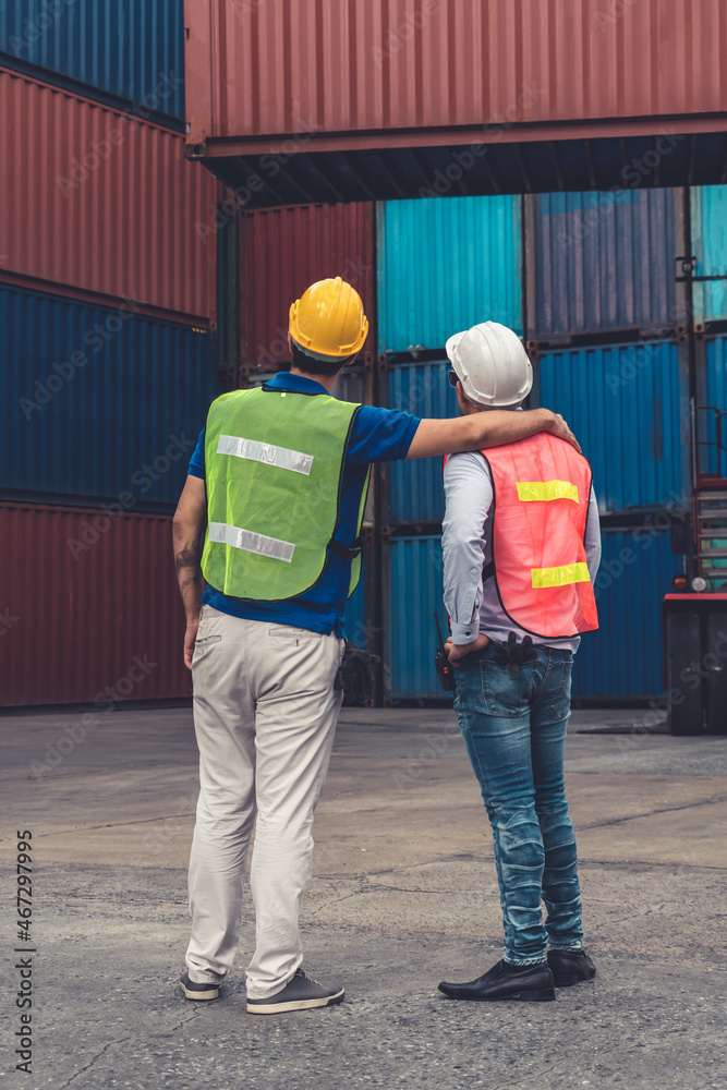 Industrial worker works with co-worker at overseas shipping container yard . Logistics supply chain 