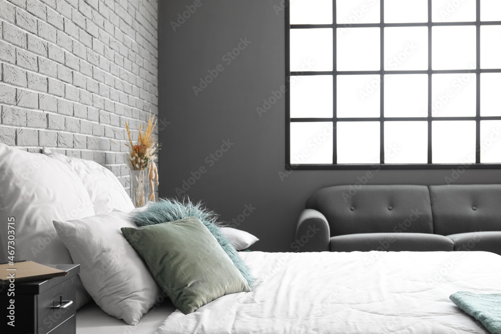 Big comfortable bed with green pillows near grey brick wall