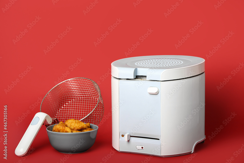 Modern deep fryer with nuggets on color background