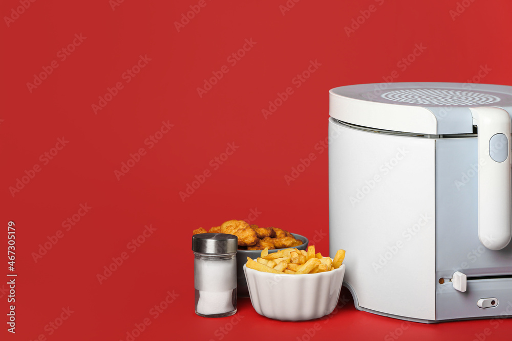 Modern deep fryer with food and salt on color background