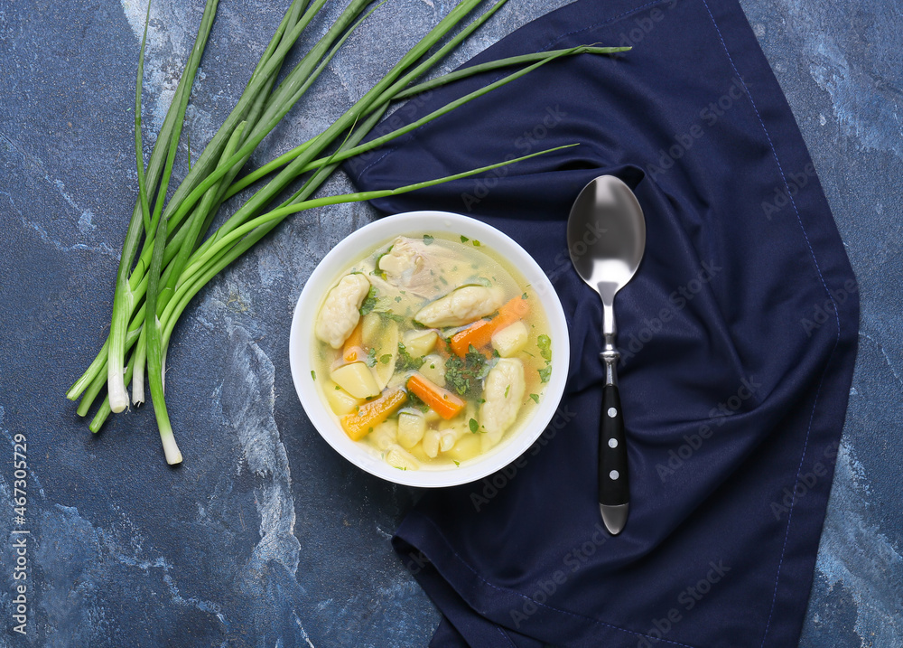 Bowl of tasty dumpling soup and green onion on color background