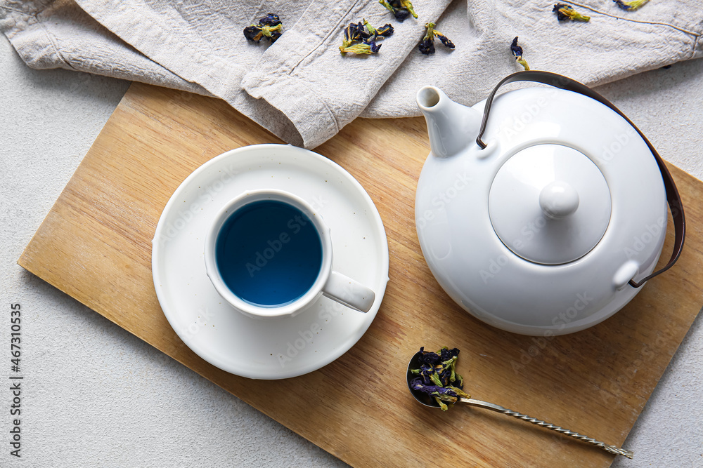 Teapot and cup of organic blue tea on light background