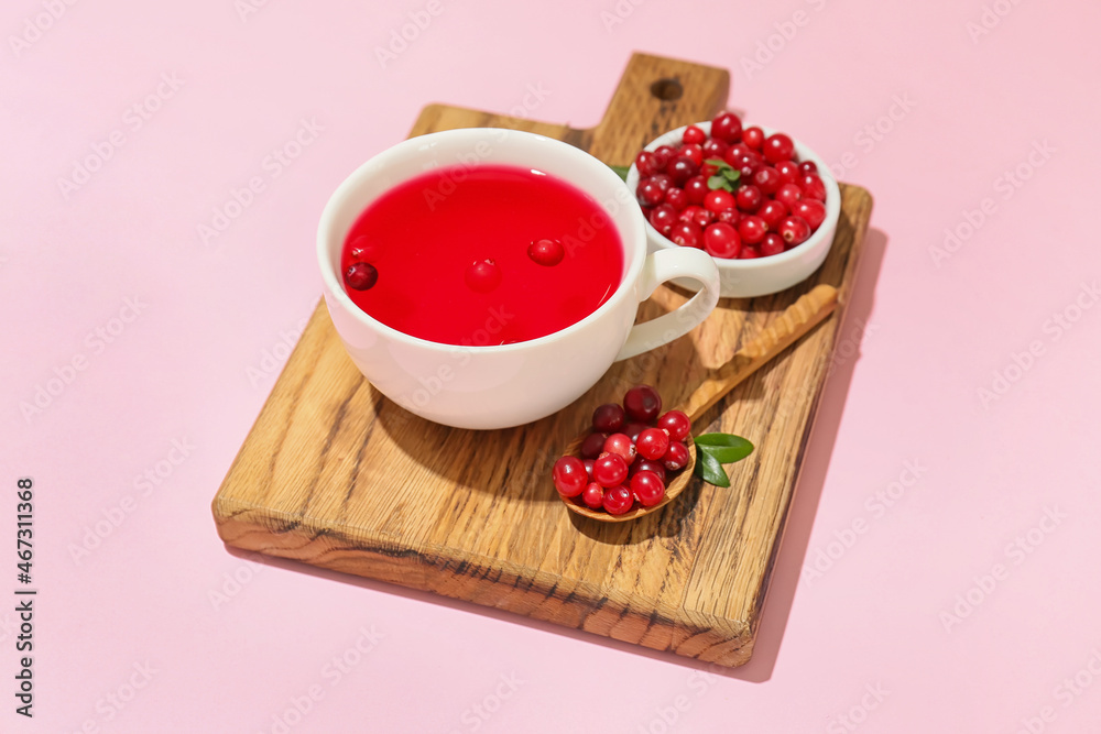 Wooden board with cup of tasty lingonberry tea and berries on color background