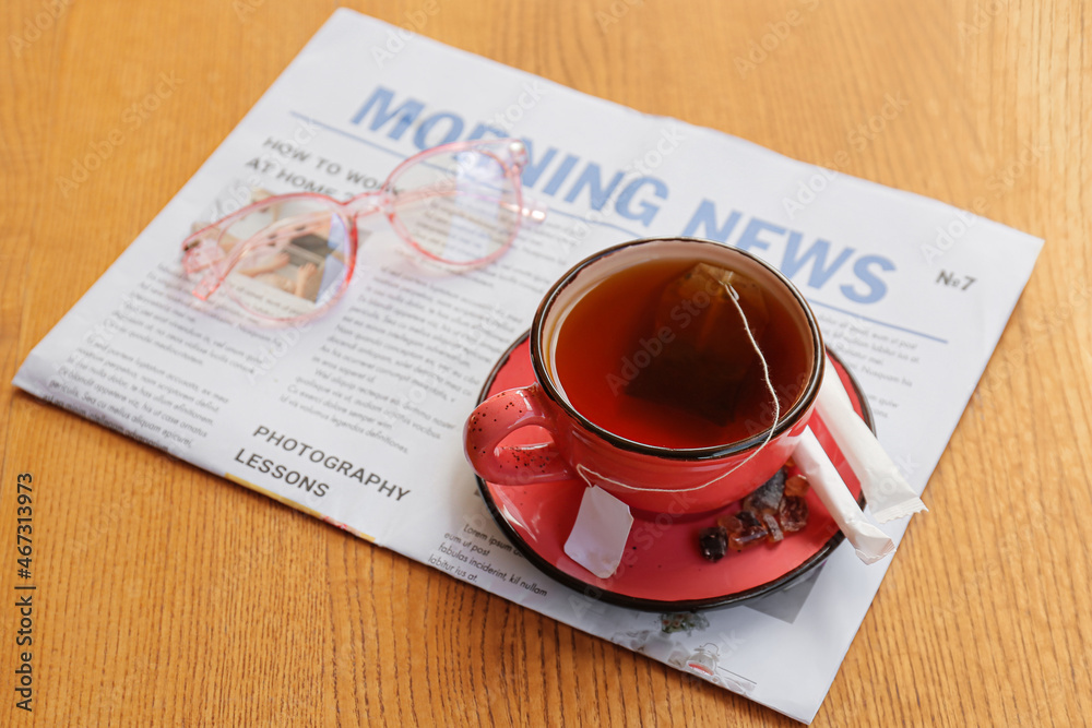 Cup of hot tea, eyeglasses and newspaper on wooden background