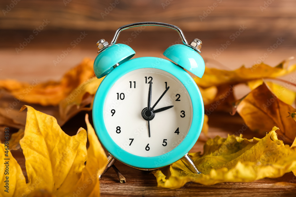 Alarm clock and autumn leaves on wooden background. Daylight saving time end