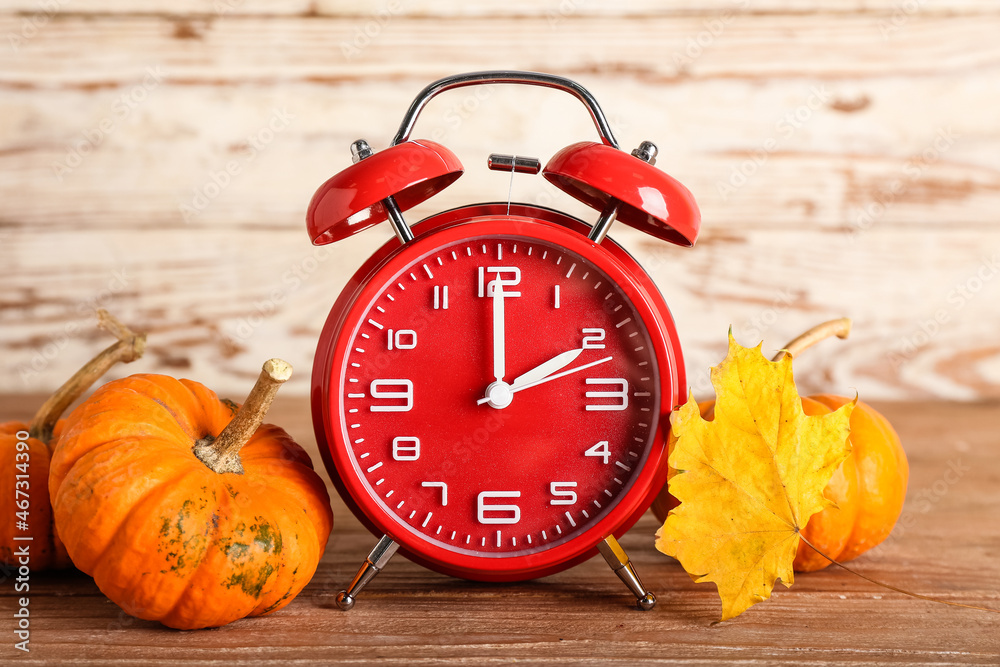 Alarm clock and autumn leaf with pumpkins on wooden background. Daylight saving time end