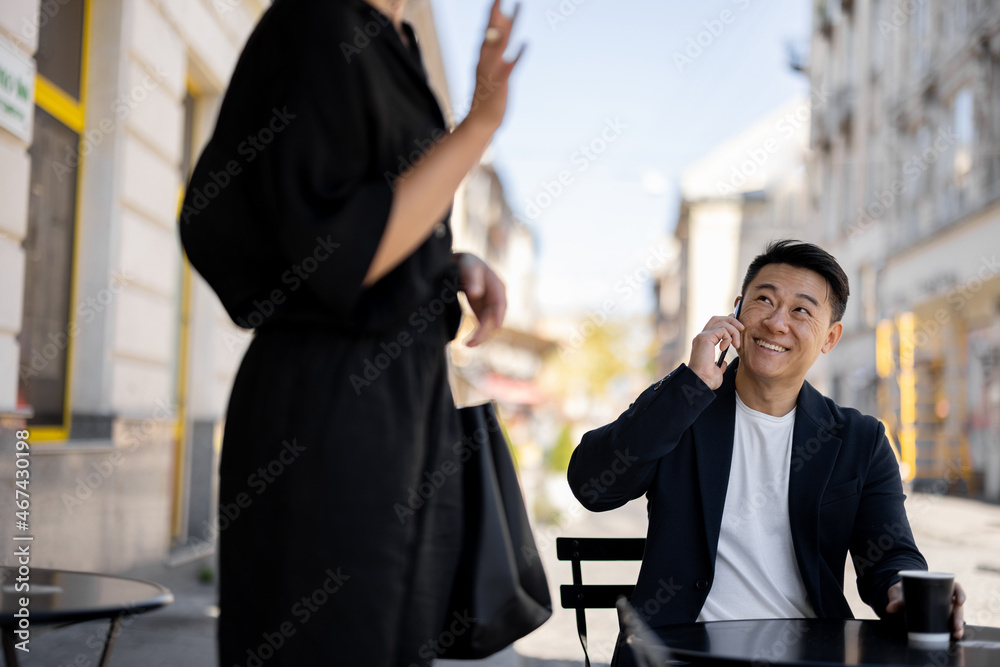 Asian businessman talking on smartphone and looking on female friend at outdoor cafe. Concept of rem