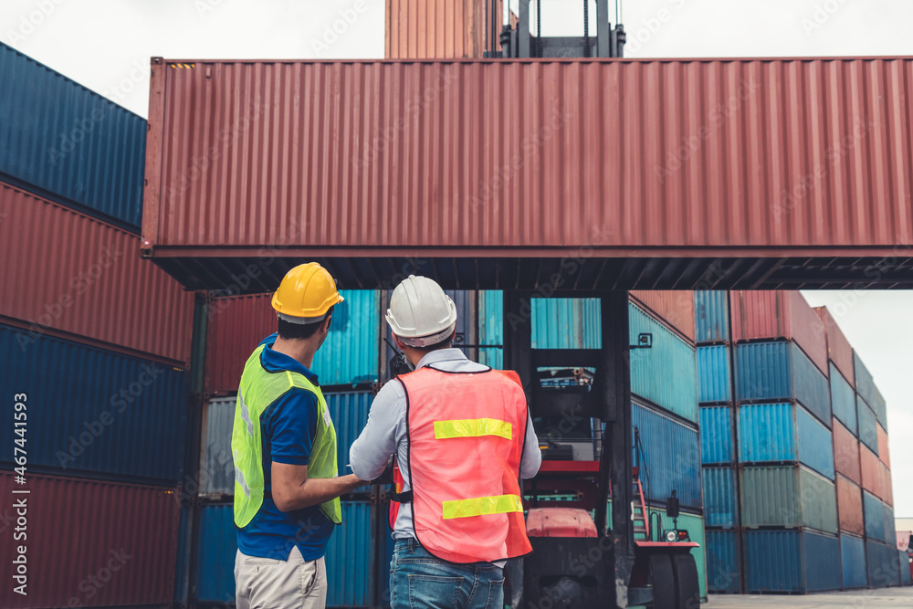 Industrial worker works with co-worker at overseas shipping container yard . Logistics supply chain 