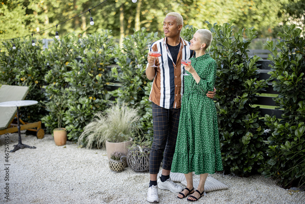 Multiracial couple drinking cocktails at home garden. European girl and black man spending time toge