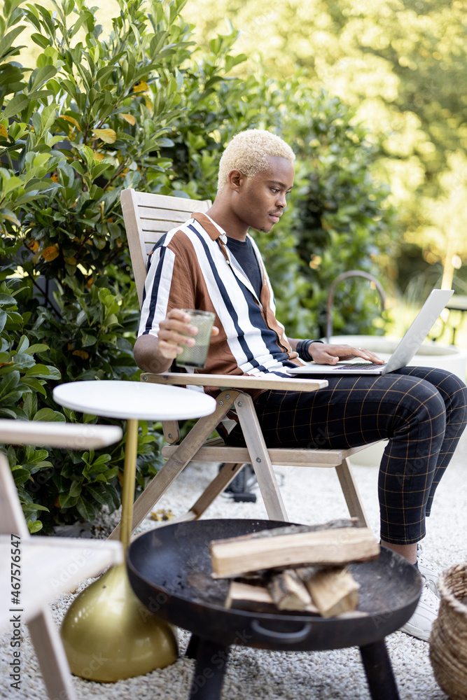 Latin man talking online or having zoom meeting using laptop computer while sitting on lounger at ho