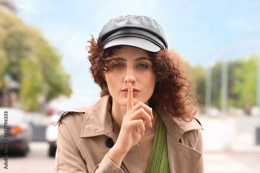 Beautiful woman in leather cap with index finger near lips in city