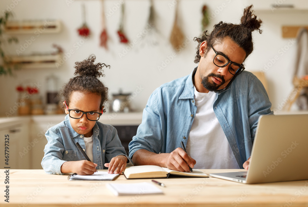 Young african american dad working remotely on laptop with child son at home