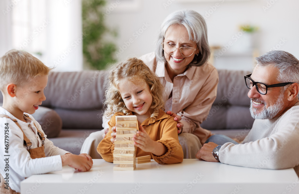 Excited children playing game Jenga at home with positive senior grandparents while sitting on sofa