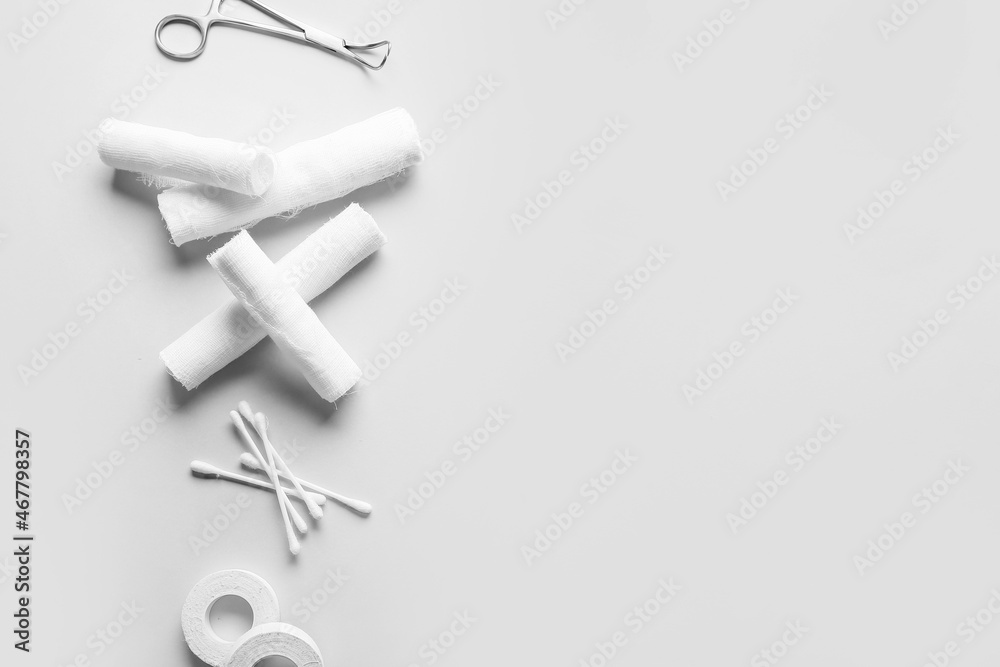 Medical plaster, cotton buds, bandage rolls and surgical tool on light background