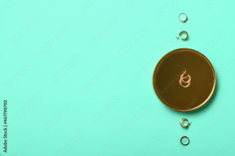 Golden tray with earrings and different jewelry on color background