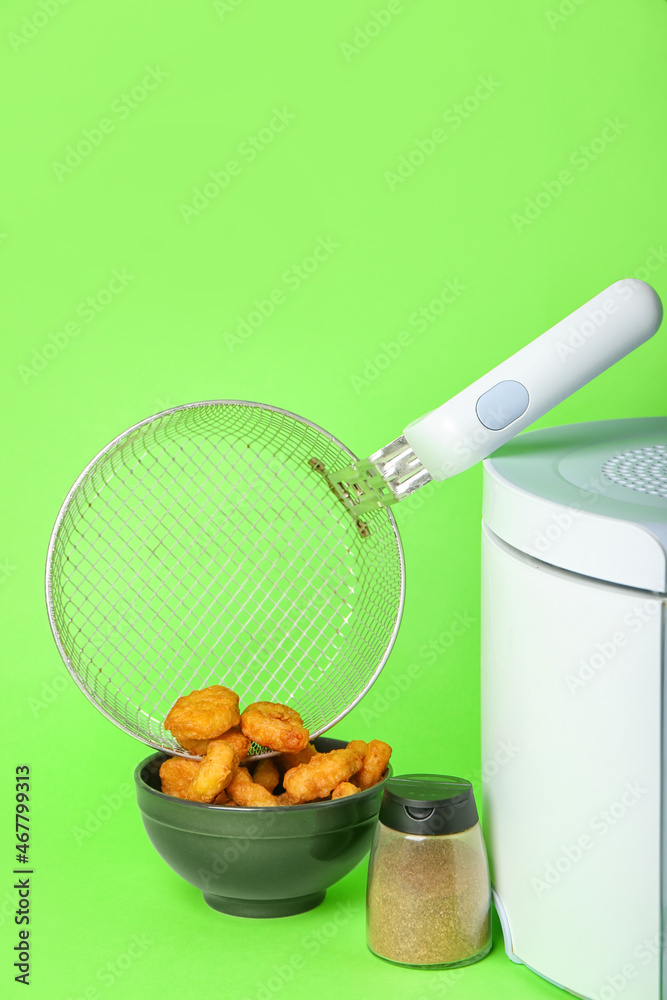 Modern deep fryer with nuggets and spices on color background