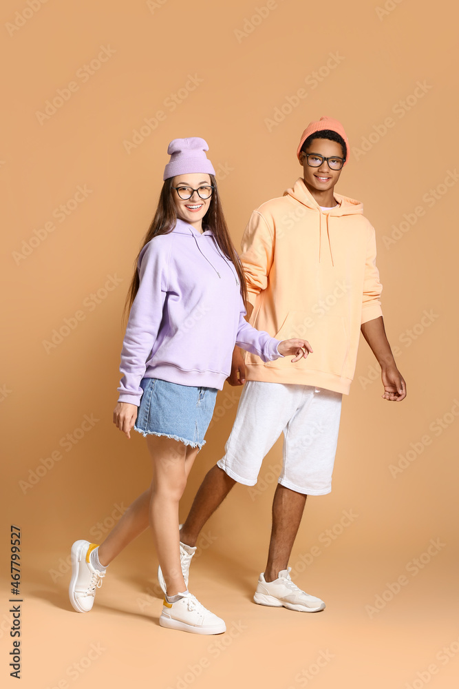 Stylish young couple in hoodies holding hands on beige background