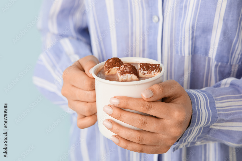 Woman holding cup of delicious cacao on color background, closeup