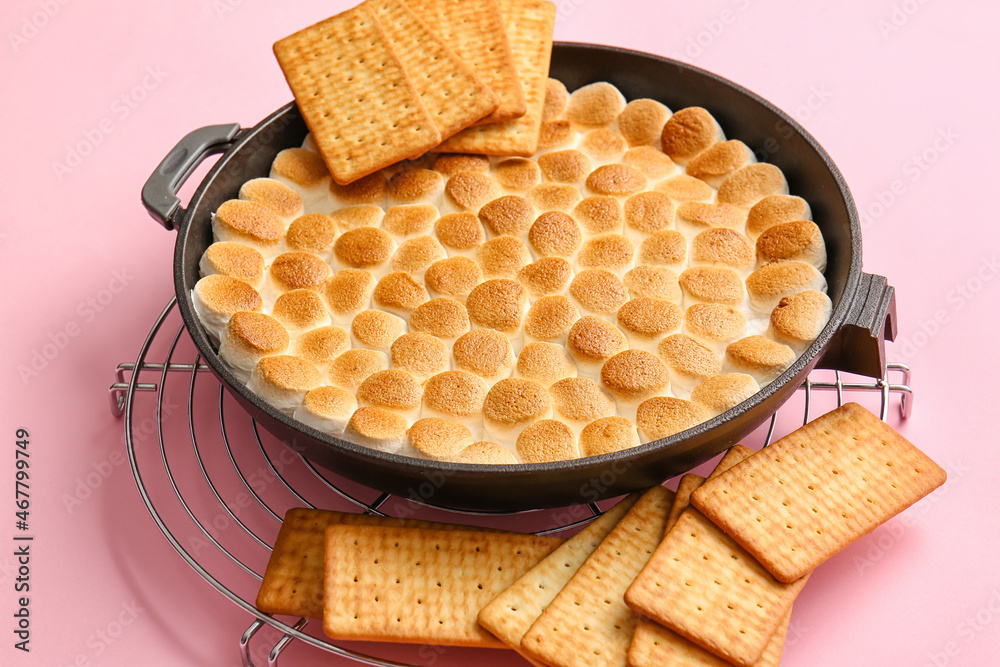 Frying pan with tasty Smores dip and crackers on pink background