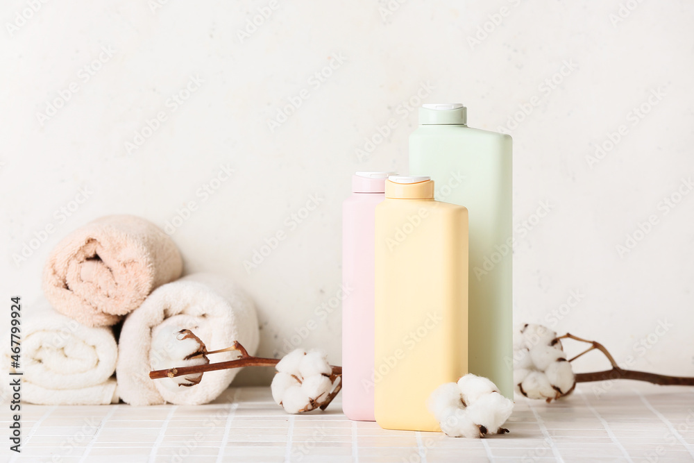 Bottles of cosmetic products, clean towels and cotton branch on tile table against light background